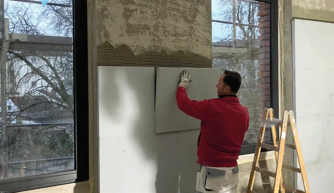 Handwerker setzt eine Kalziumsilikatplatte neben einem Fenster in das Kleberbett
