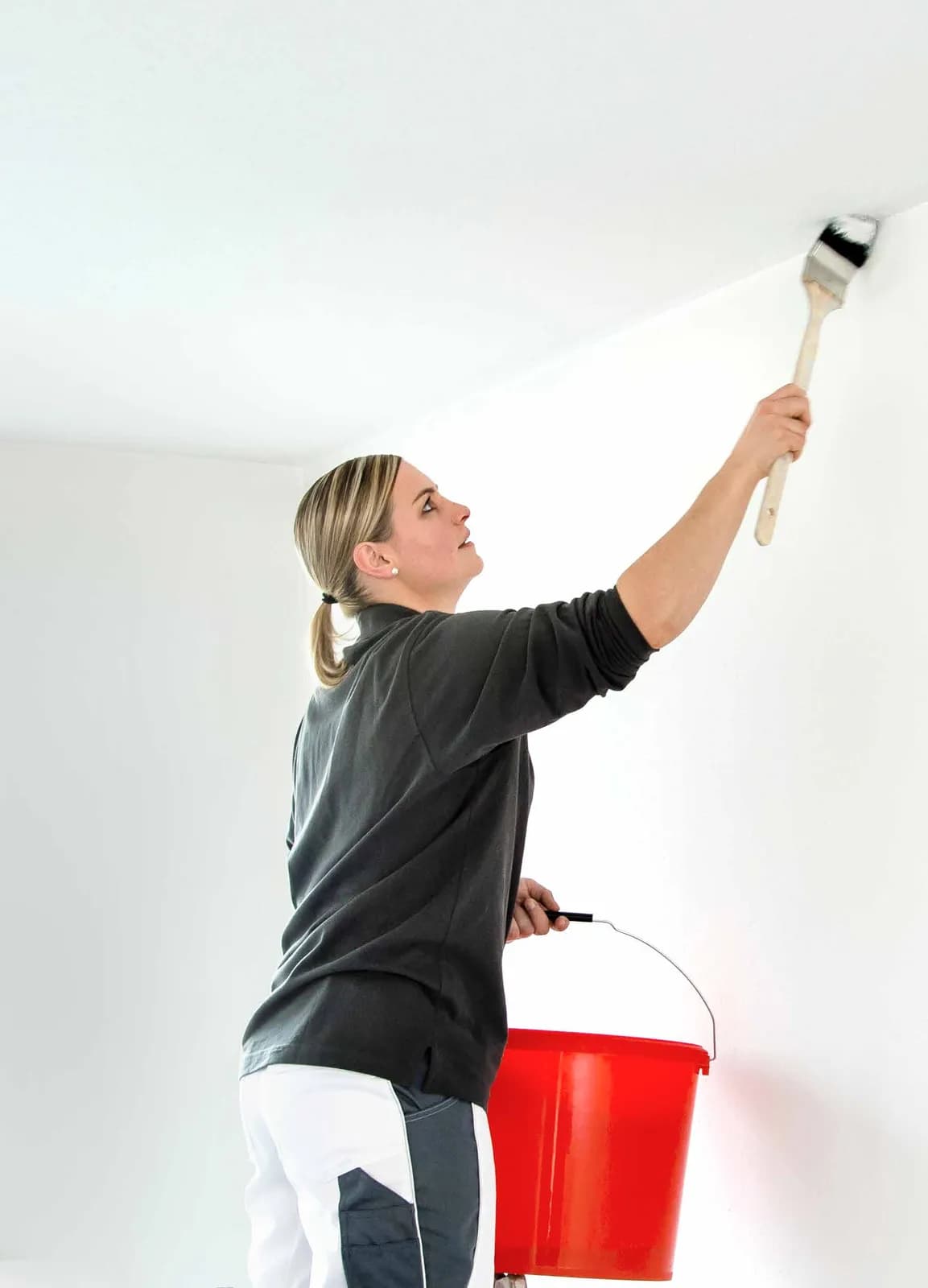 Malerin streicht mit dem Rundpinsel die Kante zwischen Wand und Decke